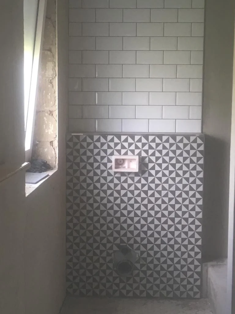 WC-Wand mit hellen Fliesen und geometrischem Mosaik